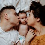 Parents lovingly kiss their newborn baby, showcasing tender family bonds.